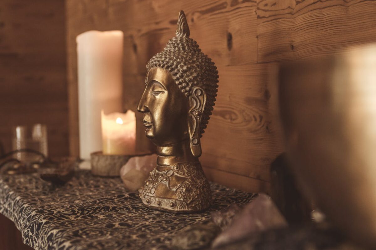 Close-up shot of a golden Buddha bust with candlelight in a serene setting.