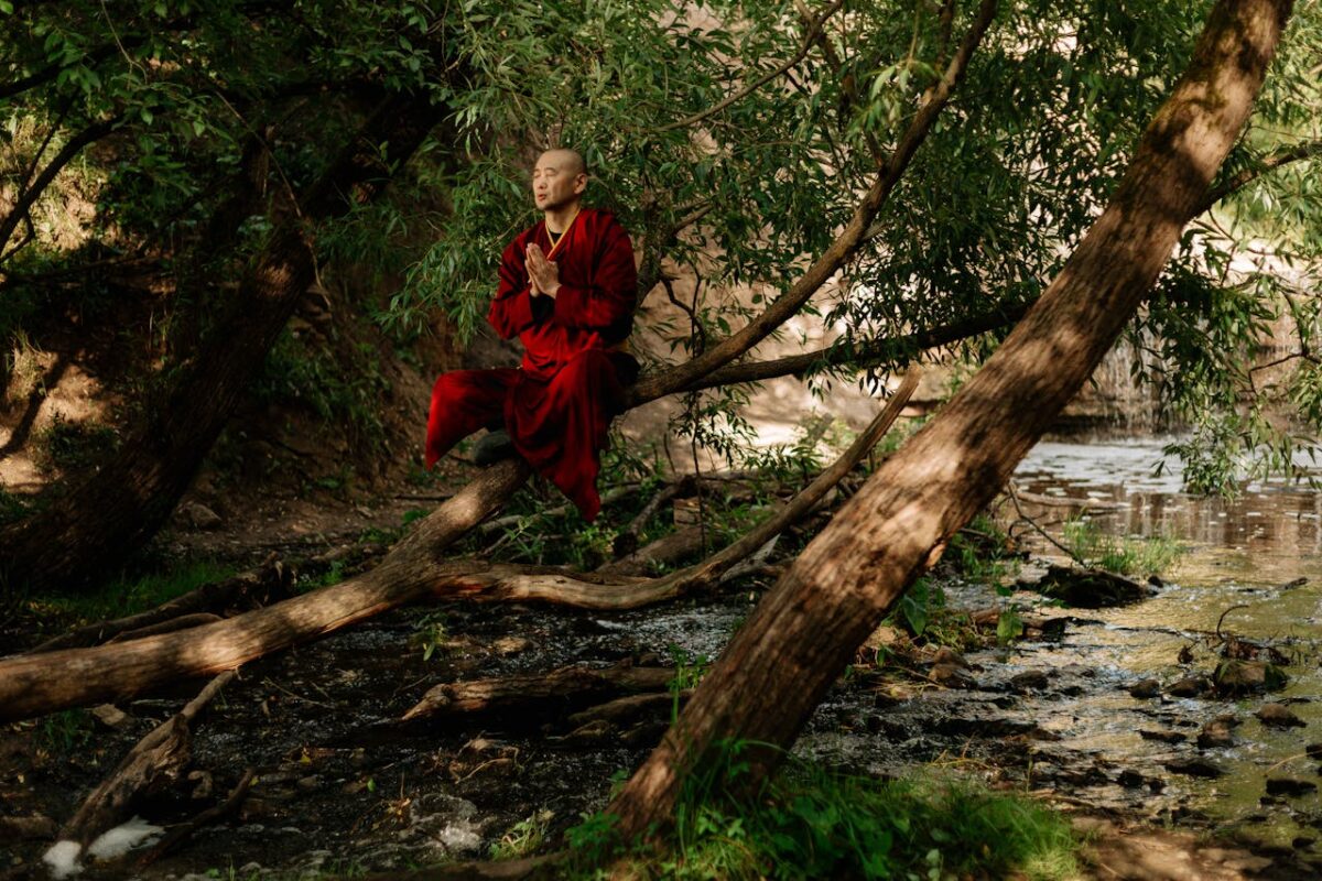 A serene monk in red robes meditates by a forest stream, embracing nature's tranquility.