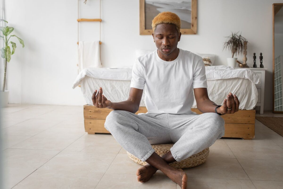 A young man practicing mindfulness meditation in a serene bedroom setting.